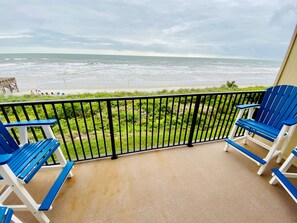 Un balcon avec deux fauteuils Adirondack bleus et blancs, un sol en béton et une vue sur l’océan.