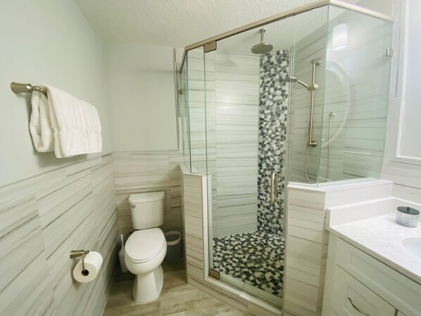 Une salle de bain moderne dotée d’une douche à parois de verre, de toilettes et d’un lavabo.