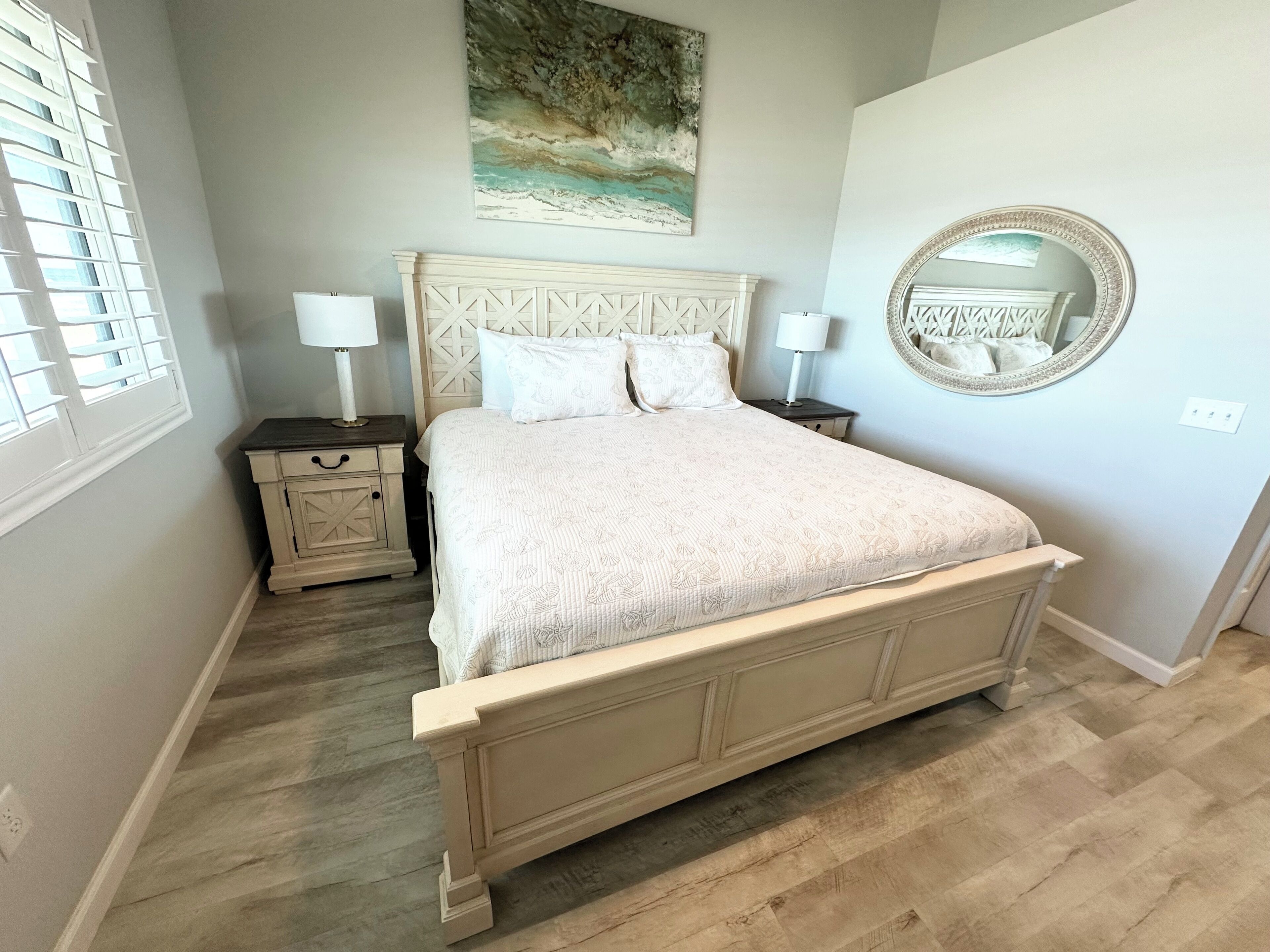 A bedroom with a bed, nightstands, a mirror, and a painting on the wall.