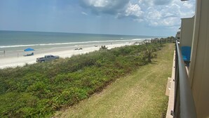 A beach view with a clear sky, a sandy beach, and a grassy area with a wooden walkway. - Oceanfront townhouse, 2 bedroom, 2.5 baths. (St. Augustine)