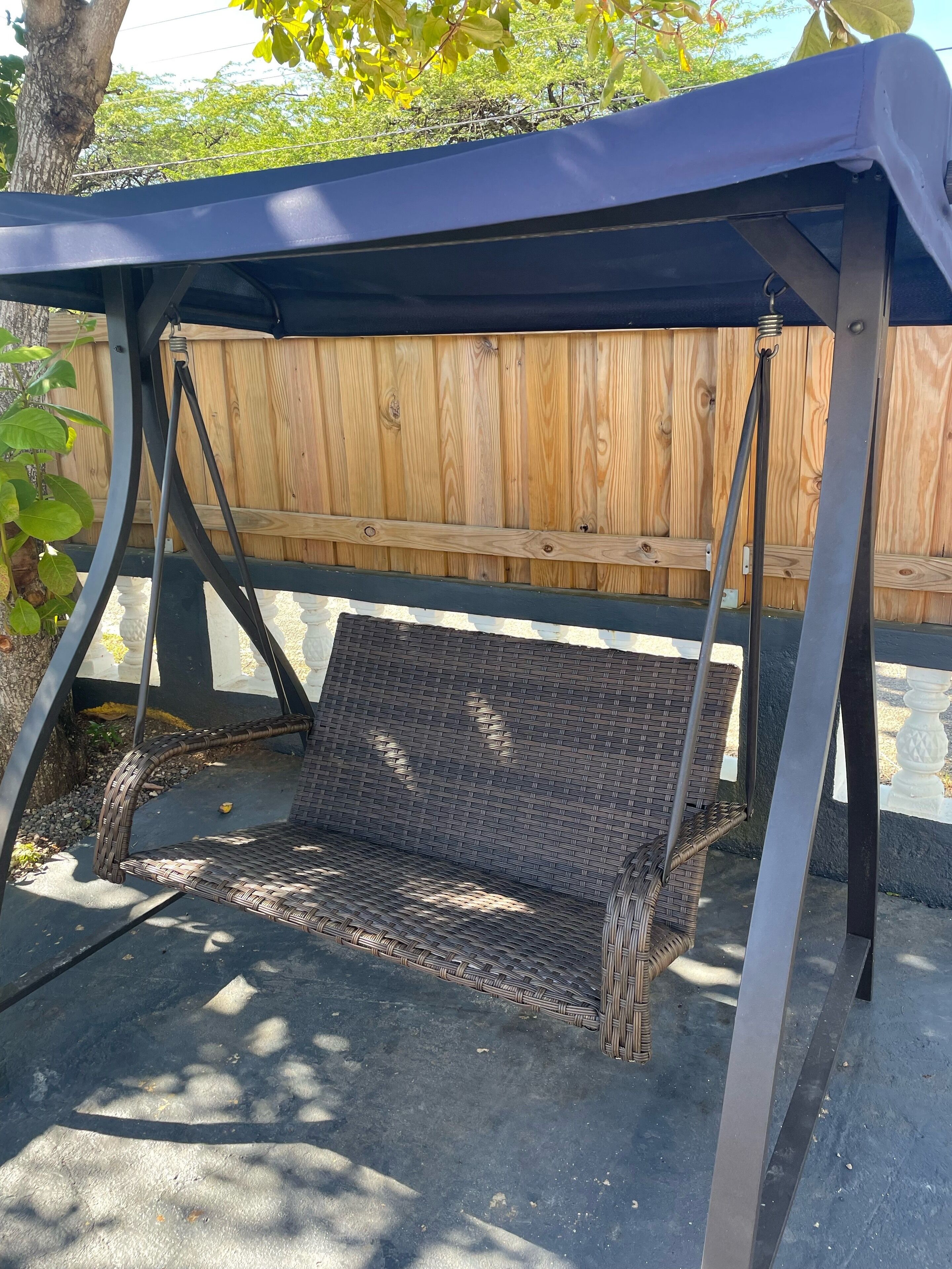 A covered outdoor seating area with a wicker bench and a swing.