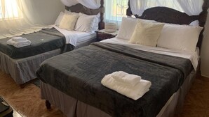 Hotellihuoneessa on kaksi sänkyä, joissa on tummat päiväpeitteet ja valkoiset tyynyt. Huoneessa on valkoiset verhot ja ikkuna, josta on näkymä.