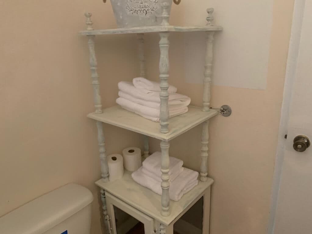 A white, antique-style shelf with towels and toilet paper in a bathroom.