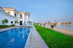 A modern house with a swimming pool, a well-maintained lawn, and a view of the water body.