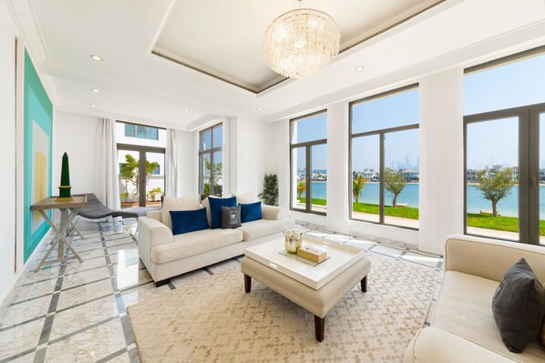 A spacious living room with a large window, a white sofa, a coffee table, and a chandelier.