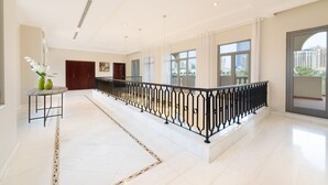 Un hall d’hôtel spacieux, doté d’un sol en marbre, d’une rampe en fer forgé noir et de grandes fenêtres offrant une vue sur la ville.