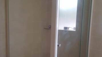 A glass-enclosed shower area with a tiled floor and a white toilet visible to the left.