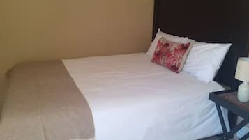Una cama con ropa de cama blanca, un cabecero oscuro y una mesita de noche con una lámpara.