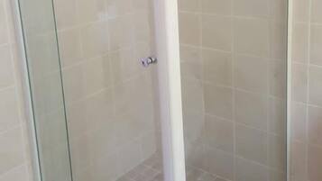 A glass-enclosed shower stall with a white frame and a tiled floor.
