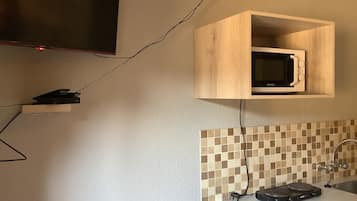 Une cuisine avec un four à micro-ondes posé sur une étagère en bois, un pare-feu en carreaux et un plan de travail sur lequel se trouve un grille-pain.