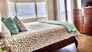 Un dormitorio con cama, cómoda, televisor y dos ventanas con persianas.