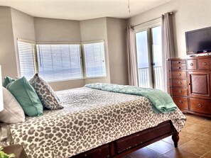A bedroom with a bed, a dresser, a television, and two windows with blinds.
