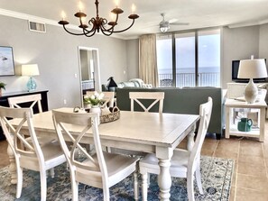 A dining area with a table and chairs, a chandelier, a view of the ocean, and a television on a stand. - Huge Beachfront Corner Unit - 2248 sq ft of bliss and paradise! (Panama City Beach)