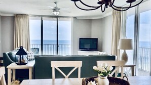Moderni hotellihuone, jossa on parveke, ruokailutila pöytineen ja tuoleineen, sohva, televisio ja kattokruunu.