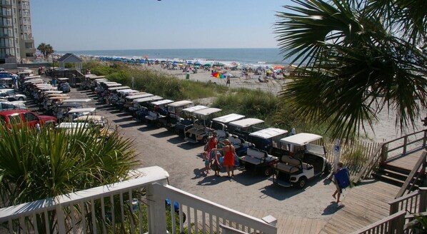 A beachside parking area with rows of vehicles and a wooden boardwalk leading to the beach.
