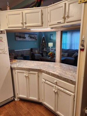 A kitchen with white cabinets, a marble countertop, and a view into a living room with a couch and a lamp.