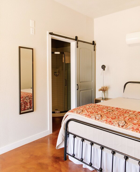 Un dormitorio con cama, espejo, puerta y zona de ducha.