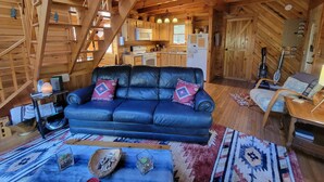 Interior acogedor de una cabaña de madera con un sofá de cuero negro, vigas de madera, una zona de cocina y un estilo rústico.