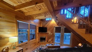 Interior acogedor de una cabaña con paredes de madera, chimenea, sofá de cuero y televisor.