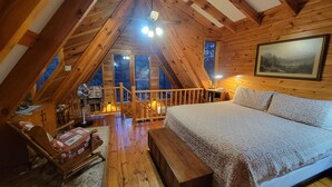 Un dormitorio acogedor en el ático, con techo de madera, una cama grande, un escritorio y vistas al exterior a través de una ventana.