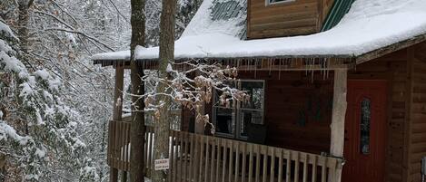 A wooden cabin with a snow-covered roof and a wooden deck.