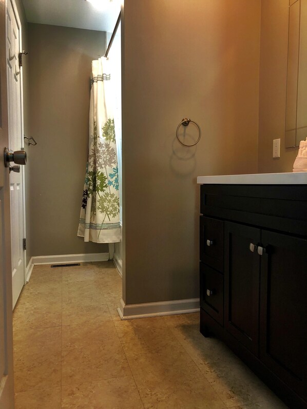 A bathroom with a shower, a towel rack, and a vanity with cabinets.