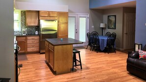 Una cocina moderna con armarios de madera y un refrigerador de acero inoxidable, un comedor con una mesa y sillas azules, y una sala de estar con un sofá de cuero.