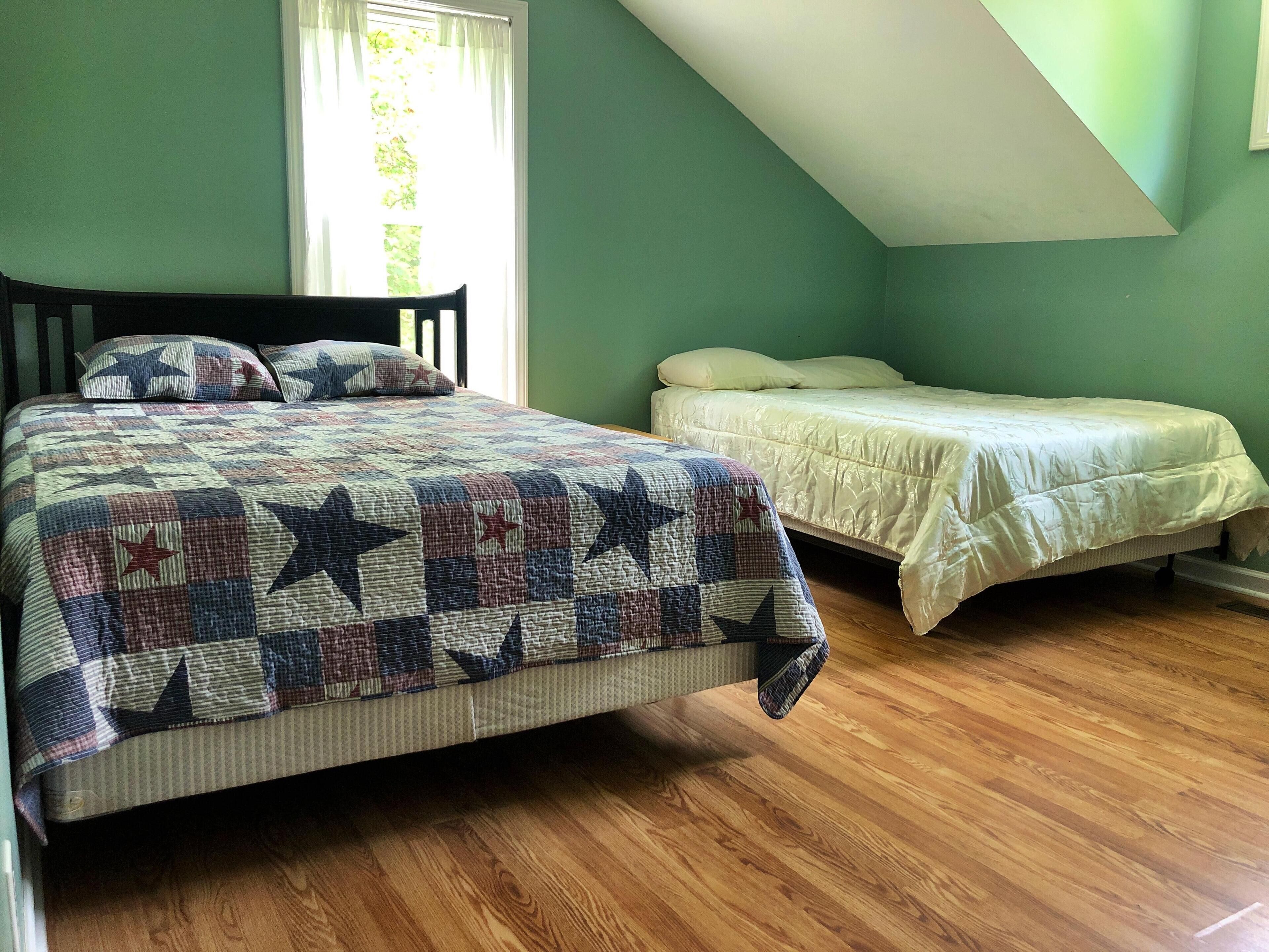 Une chambre avec un grand lit, un plus petit lit et une fenêtre avec des rideaux.