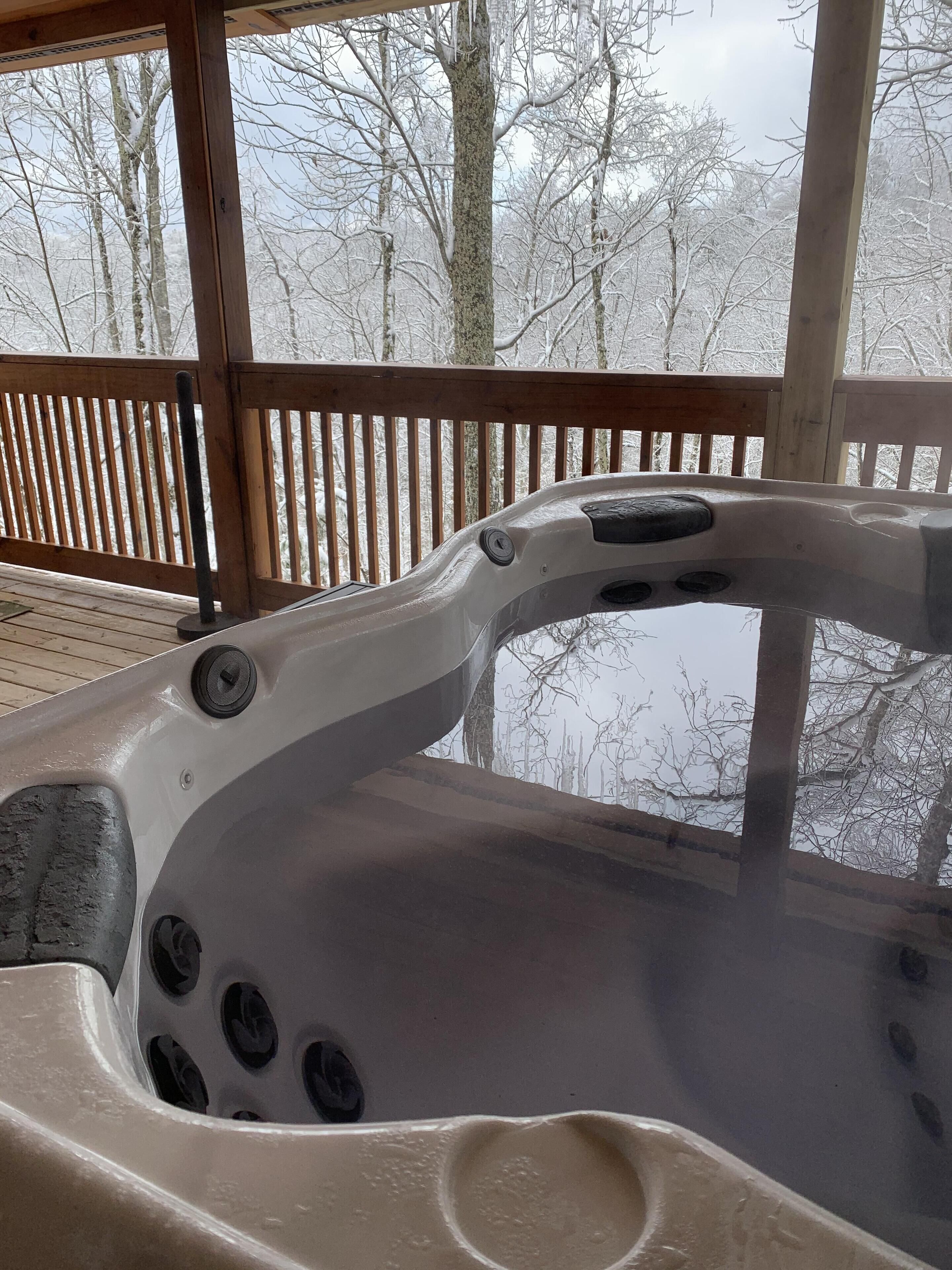 A hot tub with multiple jets, set on a wooden deck with a view of snow-covered trees.