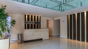 Un espace d’accueil moderne avec un comptoir en marbre, une enseigne indiquant « PAULISTA lifestyle », et un plafond en verre au-dessus.