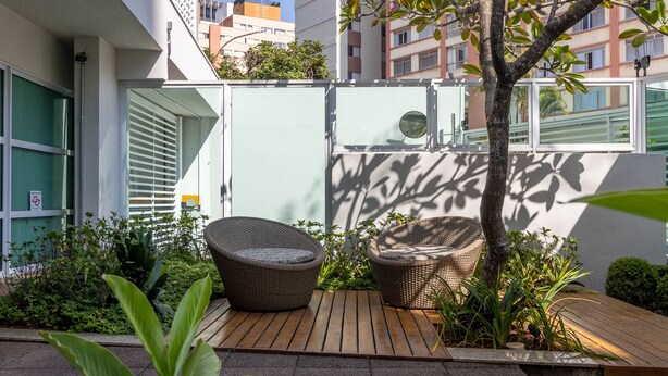 Une petite terrasse extérieure avec des meubles en osier, un arbre et une vue sur un bâtiment en arrière-plan.