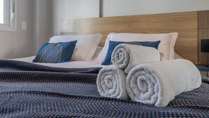 Un lit bien fait, avec des serviettes blanches pliées en rouleaux, une couverture à motifs bleus et blancs, et deux oreillers à motifs bleus et blancs.