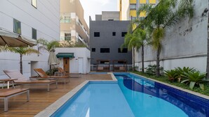 Une piscine entourée de bâtiments et de verdure, avec des chaises longues et des parasols.