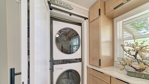 A compact laundry room with two stacked washers and dryers, wooden cabinets, and a window with blinds.