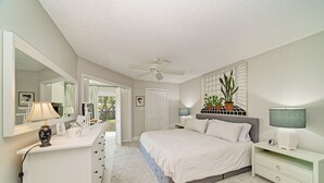 A bedroom with a bed, a dresser, a mirror, a ceiling fan, and a potted plant.