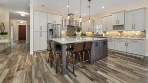 A modern kitchen with a central island, stainless steel appliances, and a herringbone wood floor. - Paradise Palm Villa- SEE OUR NEW POOL AREA AND OUTDOOR KITCHEN!  (Naples)
