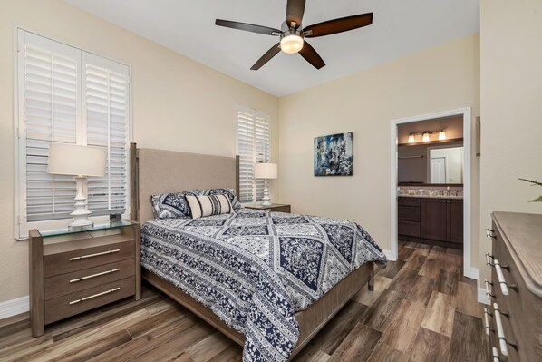 A bedroom with a bed, nightstands, a ceiling fan, and a bathroom with a vanity and mirror.