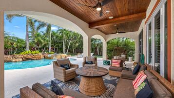Une terrasse extérieure aménagée avec des meubles en osier, une piscine et des plantes tropicales.