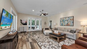 A spacious living room with a large TV, a sofa, a coffee table, and a patterned rug. - Paradise Palm Villa- SEE OUR NEW POOL AREA AND OUTDOOR KITCHEN!  (Naples)