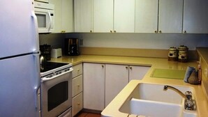 Una cucina compatta con mobili bianchi, un frigorifero in acciaio inossidabile, un forno a microonde, un forno, un lavello e una macchina da caffè.