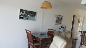 Un'area pranzo con un tavolo in vetro, due sedie in legno, una sedia imbottita bianca, una lampada a sospensione e un quadro appeso al muro.