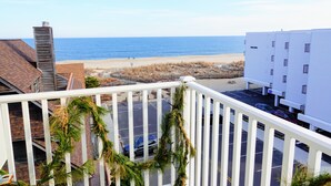 Une vue depuis un balcon donnant sur une plage, un parking et un immeuble à la façade blanche.