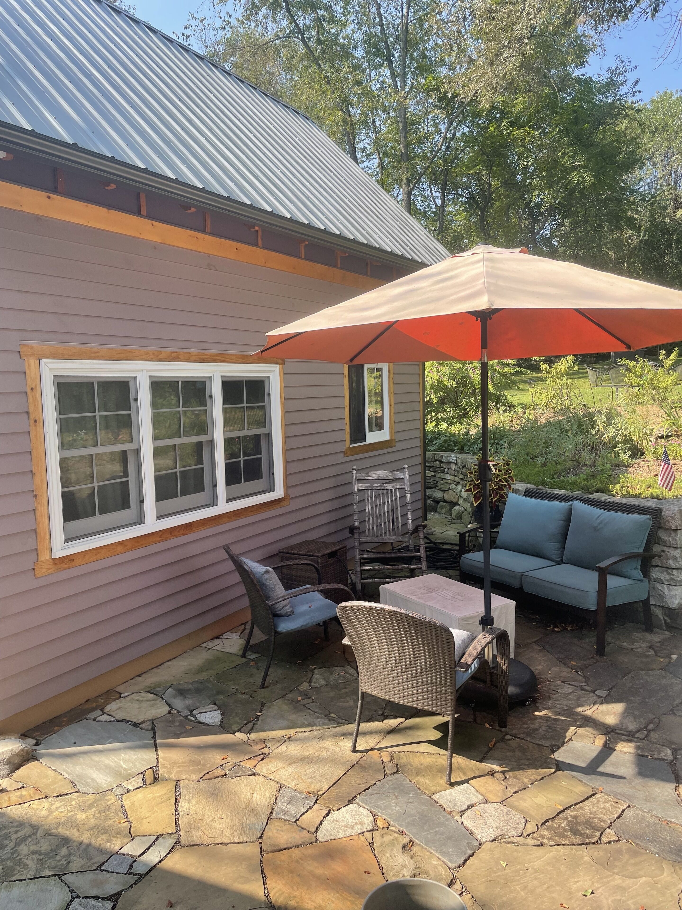 A patio with stone flooring, a wicker chair, a table, a blue sofa, and an umbrella.