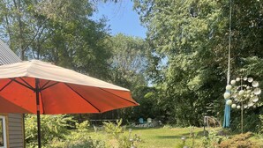 A patio area with stone flooring, outdoor furniture, and a red umbrella. - Beautiful Asheville Tiny Home Get-a-way (Asheville)