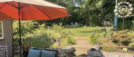 A patio area with stone flooring, outdoor furniture, and a red umbrella.