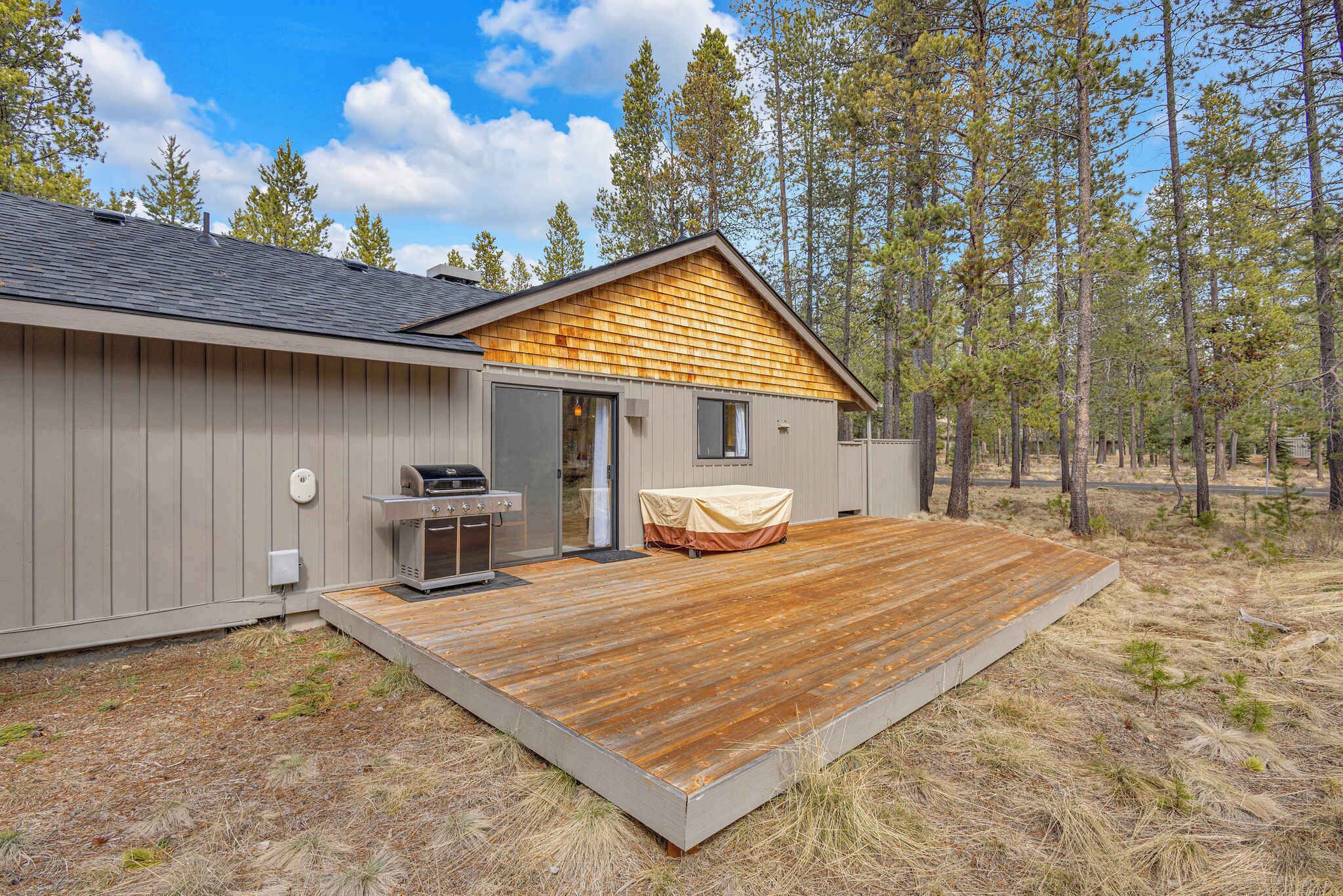 A cabin with a deck, a grill, and a covered seating area.