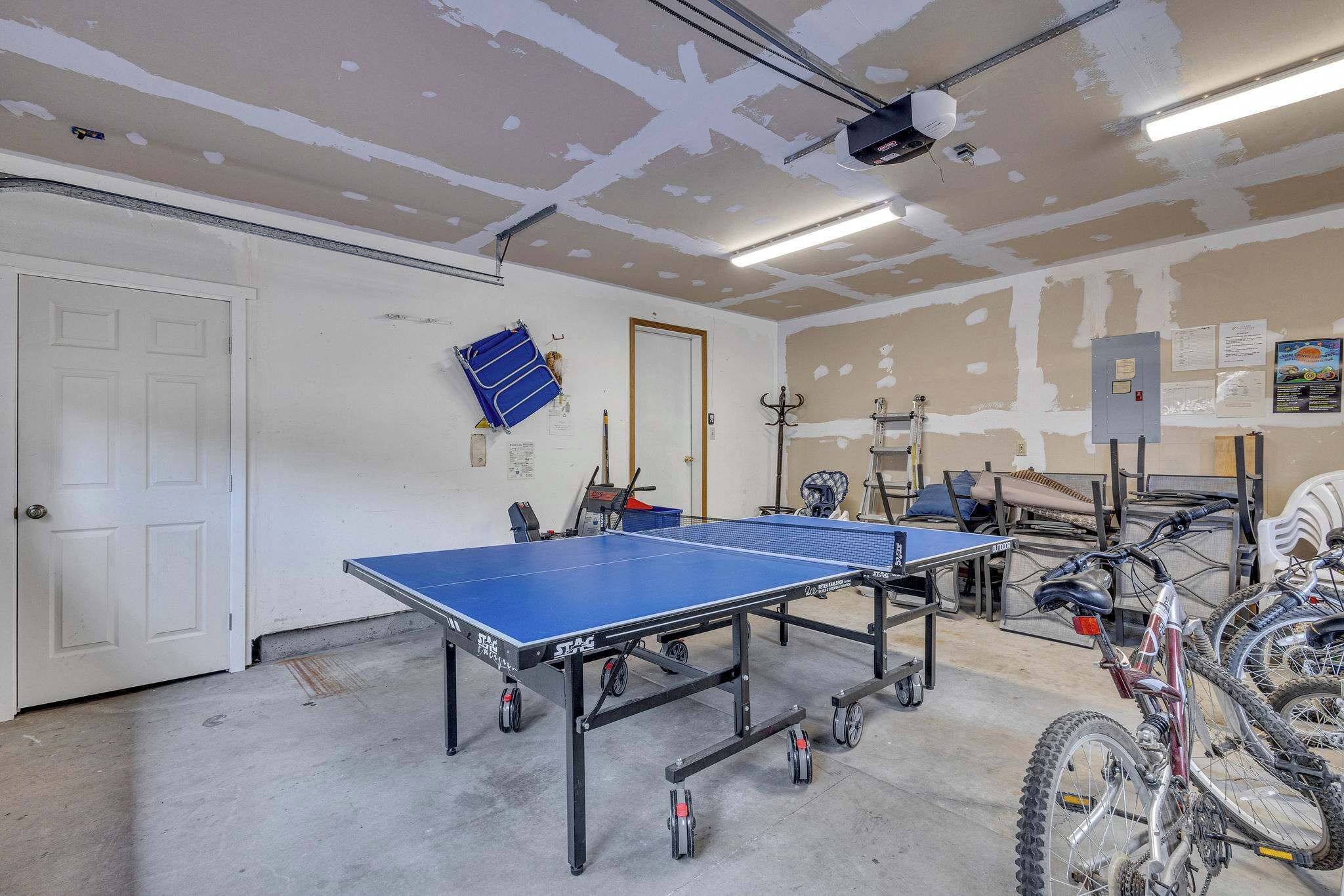 A room with two ping pong tables, bicycles, and a door.