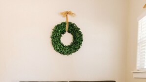 Un salon avec un canapé gris foncé, une table basse en bois sur laquelle sont posés des magazines, une couronne verte accrochée au mur et un tapis à motifs.