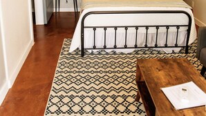 Une chambre à coucher comprenant un lit, des tables de chevet, une commode, un banc en bois, un tapis à motifs et un climatiseur fixé au mur.