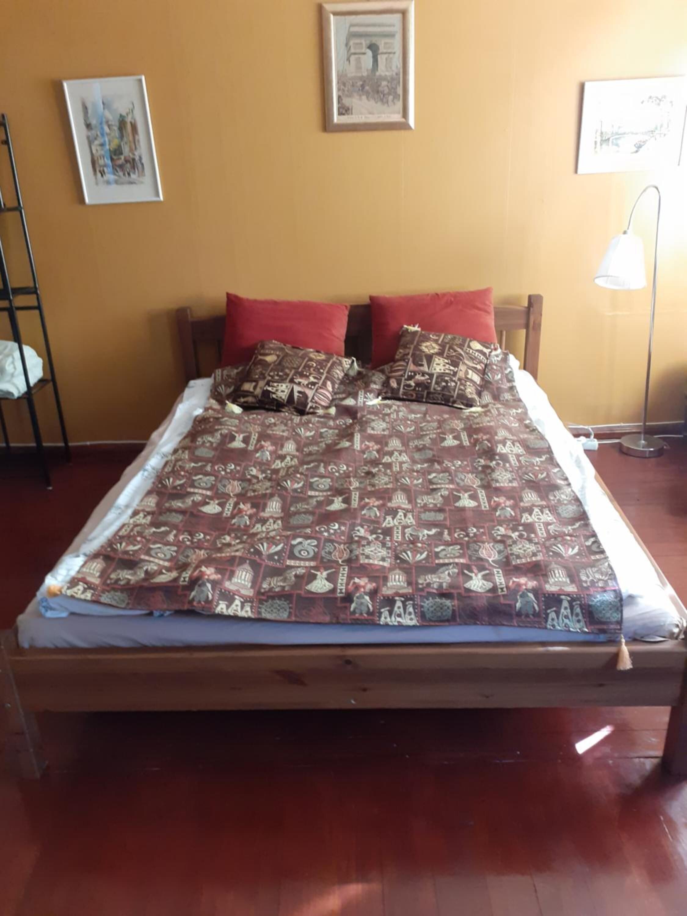 A bed with a patterned bedspread, two red pillows, and a wooden headboard.